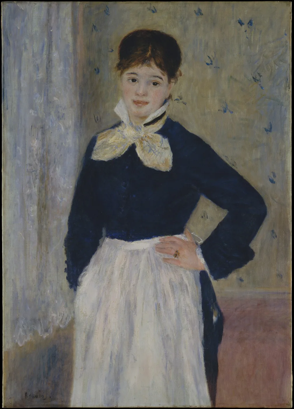 A waitress in a dark blue jacket and white apron standing with a hand on her hip, before a wall patterned with small blue swallows