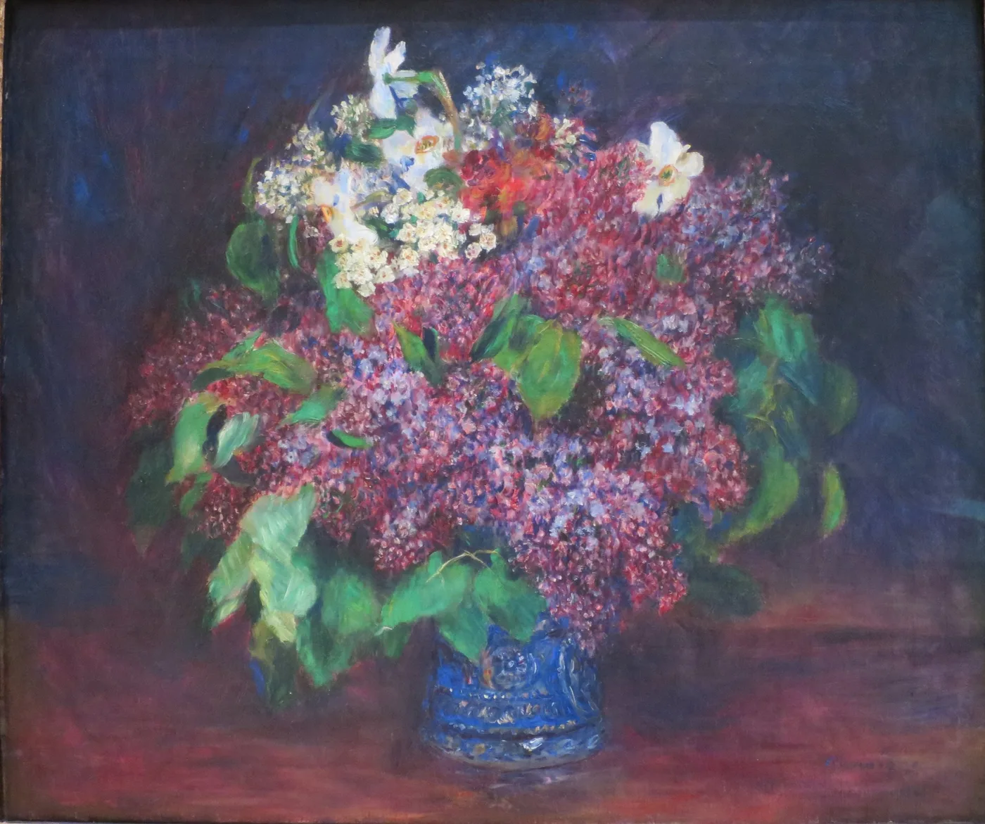 A full bouquet of purple and white lilacs in a blue vase, set against a dark background with a deep red tabletop