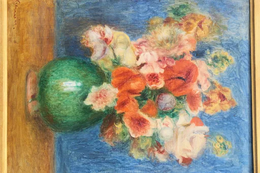 A still life of a mixed bouquet of orange poppies, pink roses and yellow blooms in a round green vase on a wooden table, against blue