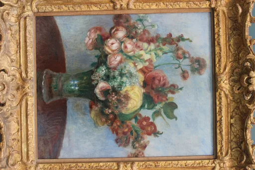 A tall bouquet of pink roses, white blossoms, and red flowers in a green glass vase on a table, against a pale blue background