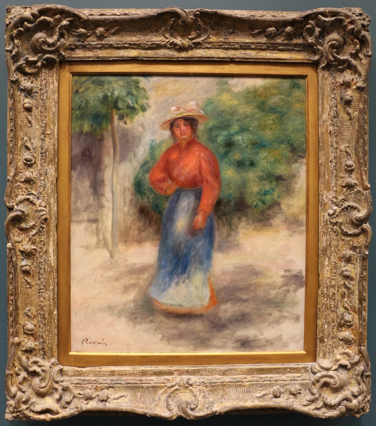 A woman in a straw hat, red blouse, and blue skirt standing on a garden path amid green foliage, in warm orange and blue tones