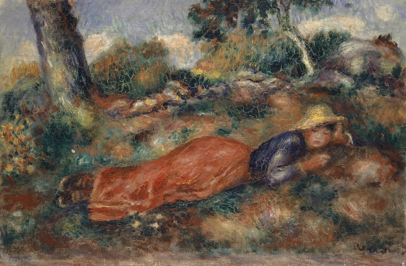 A girl in a straw hat lies face down on the grass under a tree, wearing a red skirt and dark blue top.