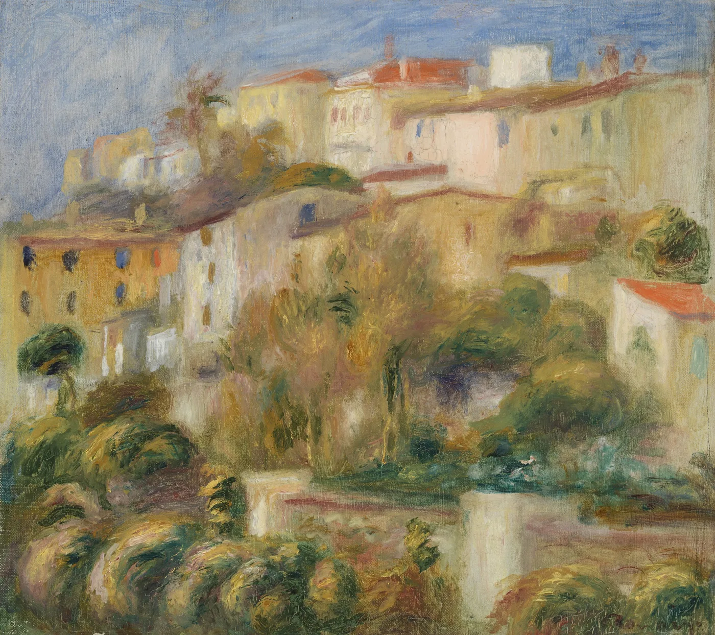A hillside village of cream and terracotta houses rises above lush green shrubs under a pale blue sky.
