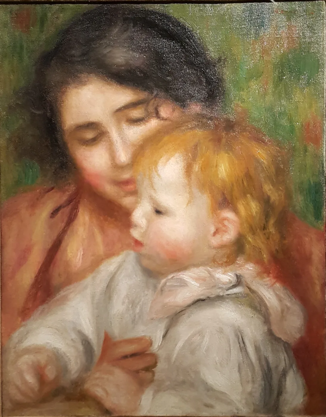 A dark-haired woman in a rust-orange wrap cradles a blond toddler in a white smock close to her cheek, against a soft green background.