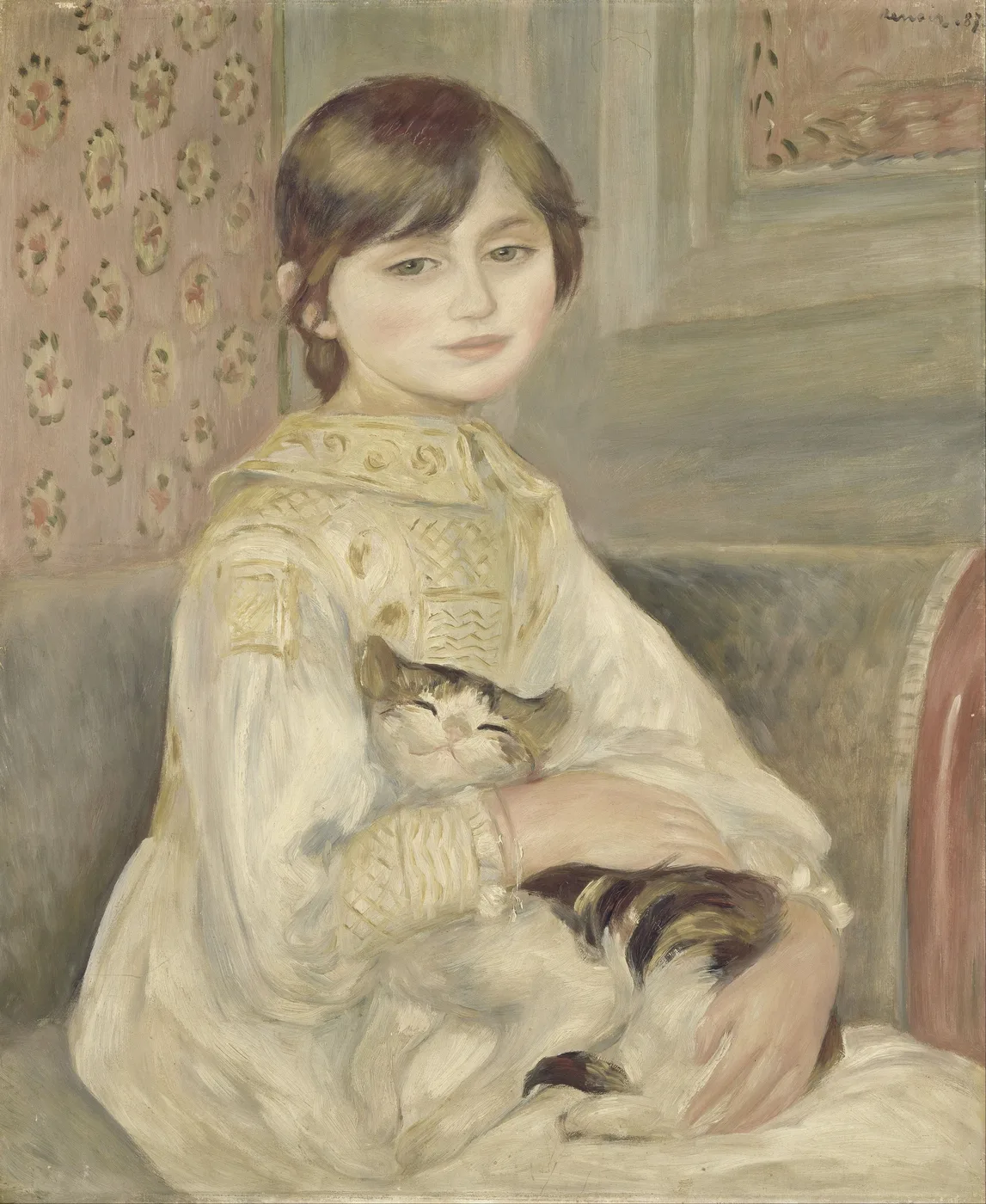 A young girl in a cream embroidered dress seated indoors, cradling a sleeping tabby and white cat in her arms, before pink floral wallpaper