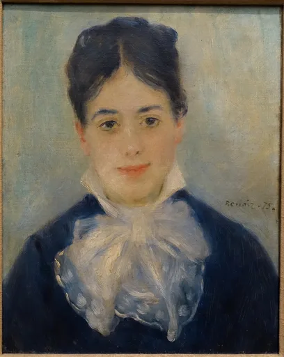 A smiling dark-haired woman in a navy jacket with a large frilled white collar, portrait against a pale blue-grey background
