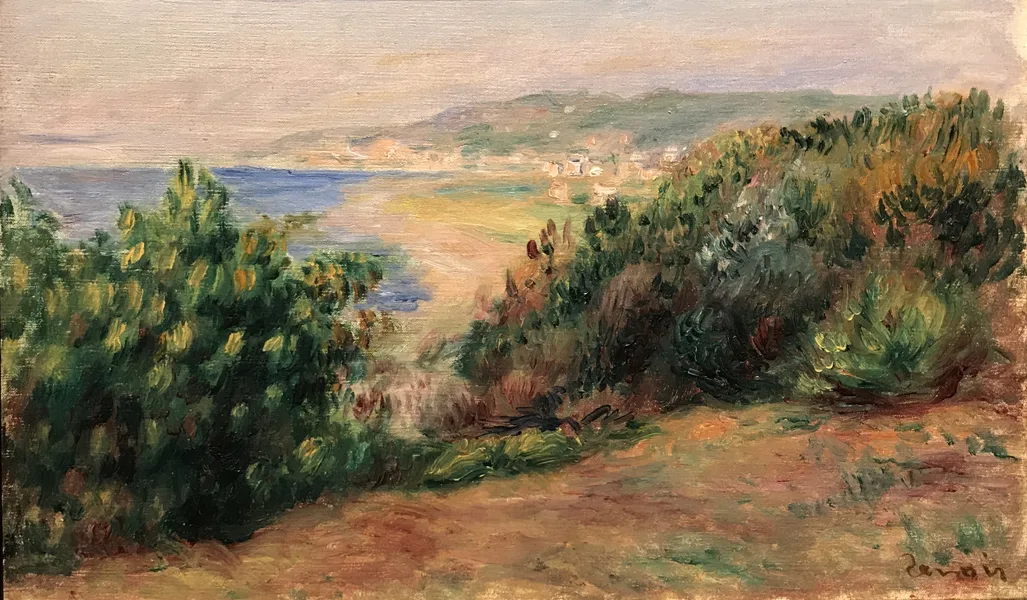 A coastal path opens between green and ochre shrubs toward a blue sea and a distant hazy coastal town.