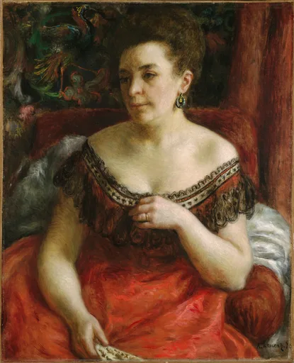 A woman in an off-shoulder red dress trimmed with black lace wears a drop earring, seated before a dark screen.