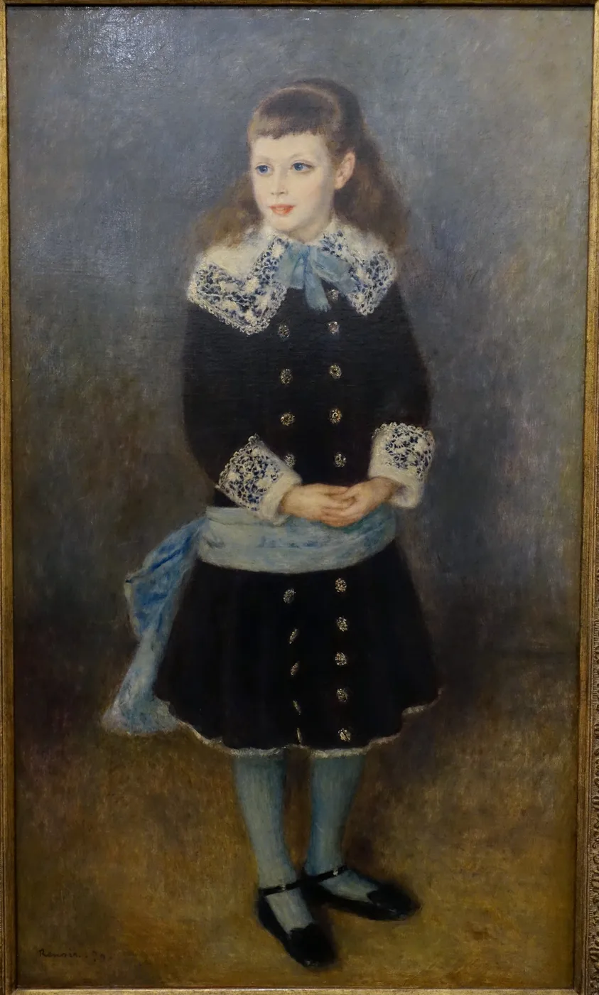Full-length portrait of a young girl in a dark dress with lace collar and cuffs, blue sash and stockings, hands clasped, plain backdrop.