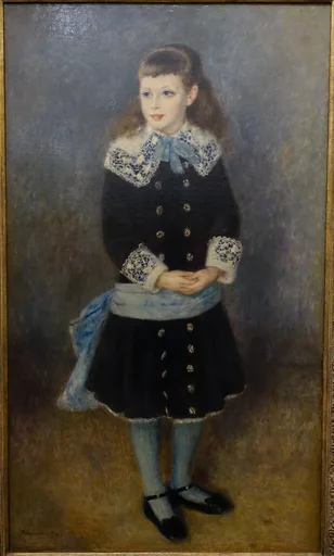 Full-length portrait of a young girl in a dark dress with lace collar and cuffs, blue sash and stockings, hands clasped, plain backdrop.