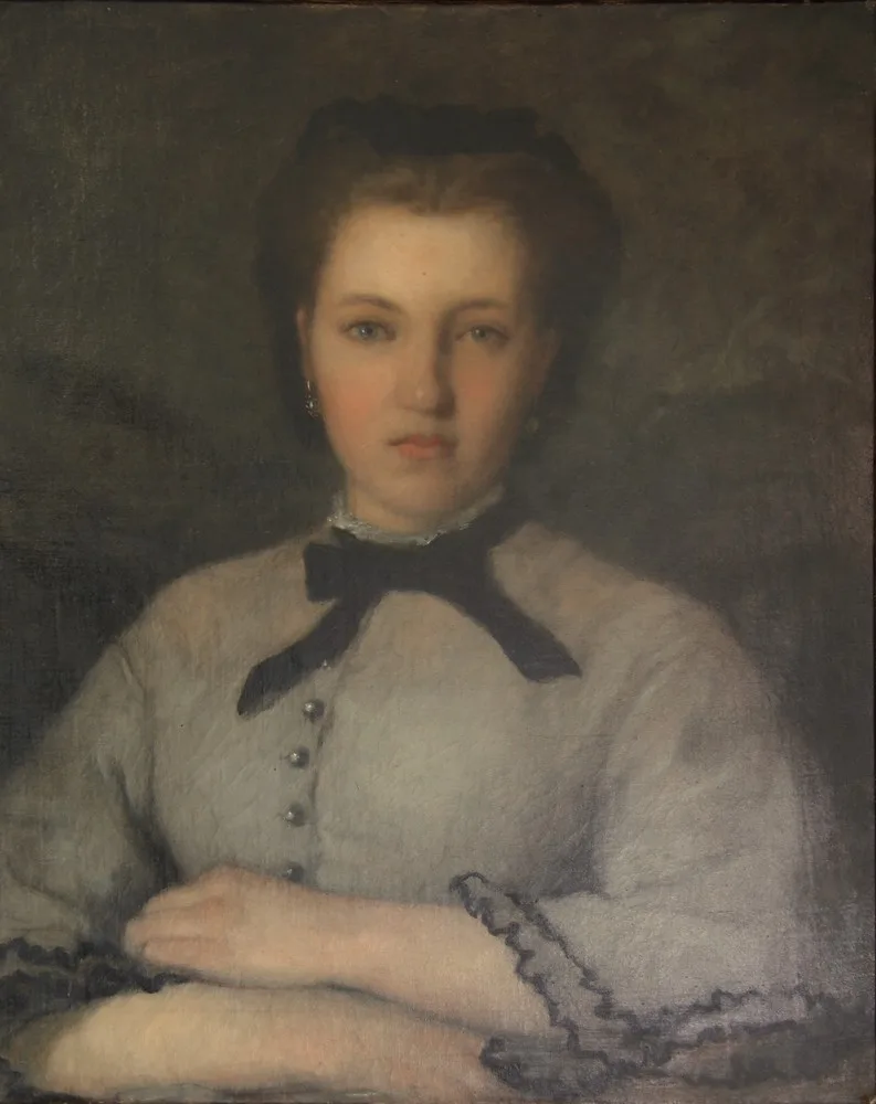 A young woman with dark hair pulled back gazes forward, wearing a pale grey dress with a black bow at the collar, hands folded.