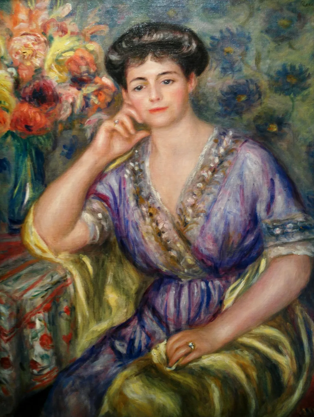 A seated woman in a purple and gold gown resting her chin on her hand beside a vase of flowers, in lavender, gold, and rose tones