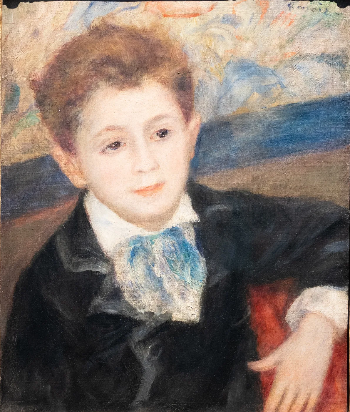 A red-haired young man in a black jacket with a blue cravat rests his hand on a red armchair, painted in black, pale blue, and warm skin tones.