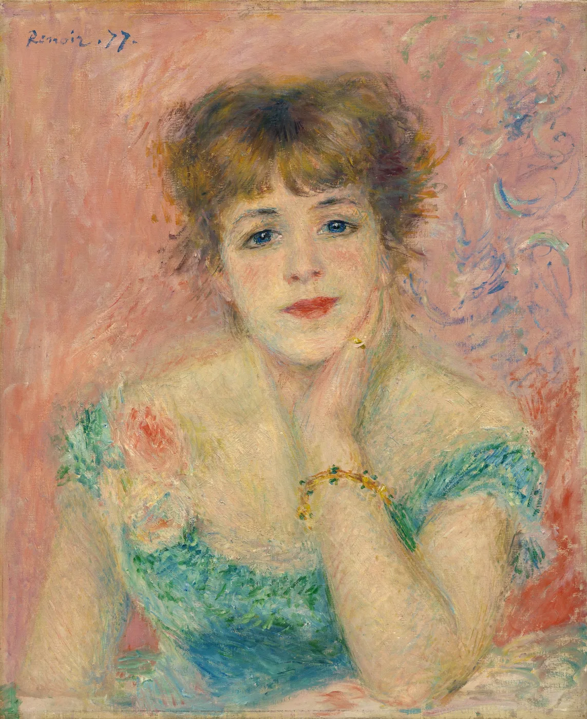 A young woman with tousled auburn hair rests her chin on her hand in a soft green dress against a pink background