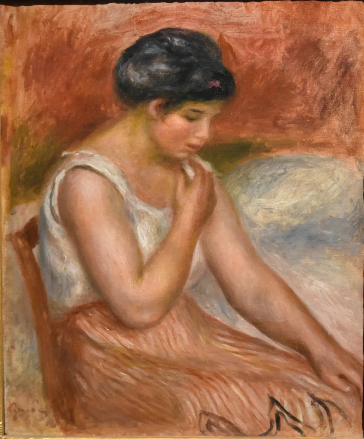 A seated girl in a white blouse and orange skirt looks down thoughtfully with hands clasped, against a warm terracotta background.