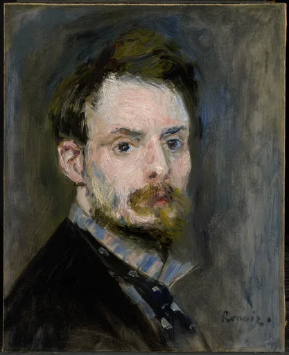 A young bearded man with tousled brown hair looks intently at the viewer, wearing a dark coat over a striped blue shirt, against a grey background