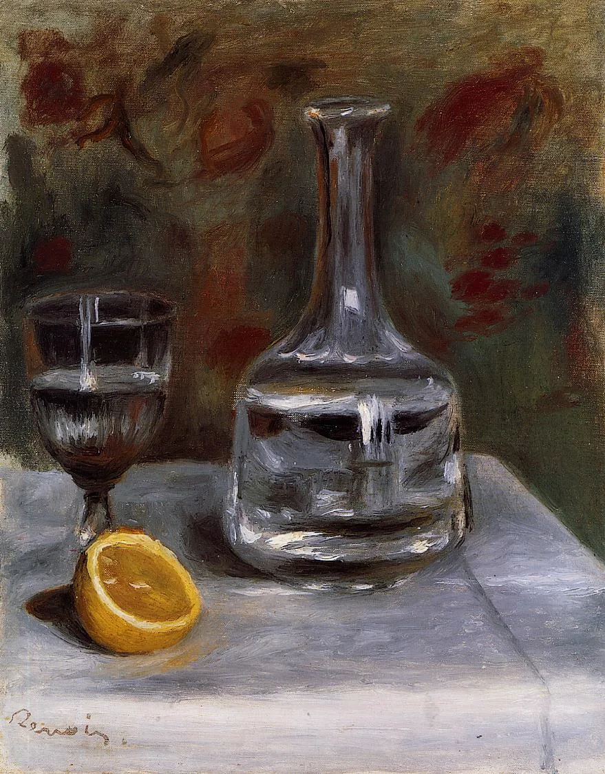 A glass carafe and stemmed glass stand beside a halved orange on a white tablecloth, dark floral pattern behind.