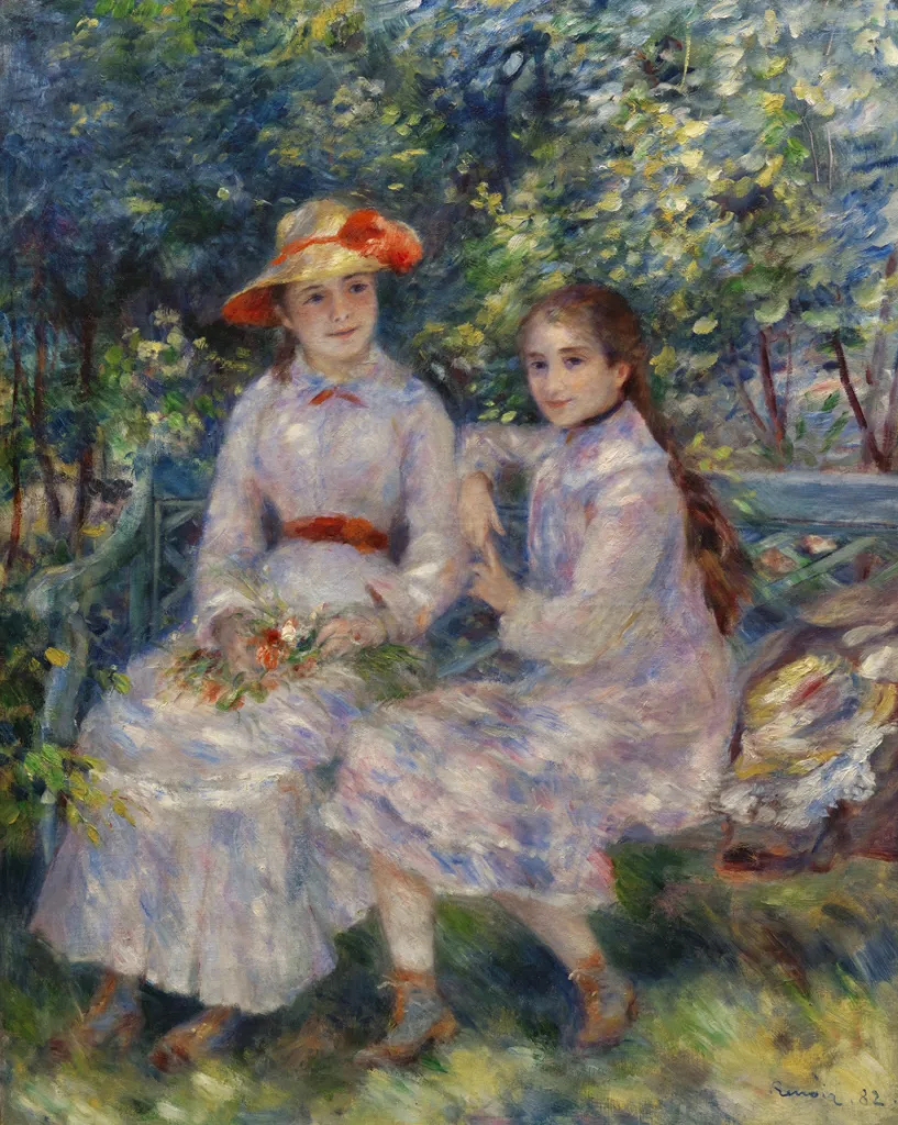 Two young girls in pale floral dresses sit together on a garden bench, one in a straw hat with an orange ribbon holding flowers.