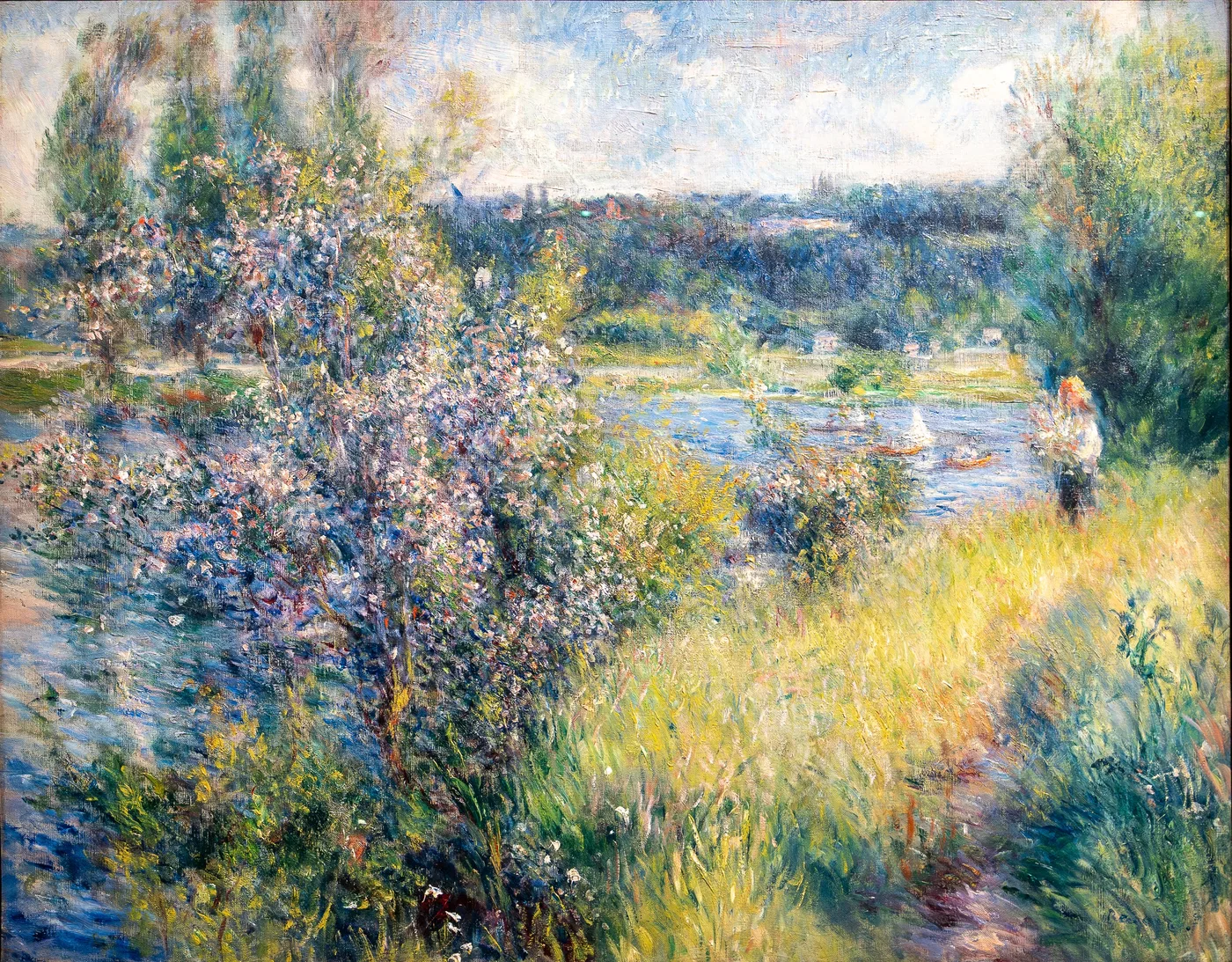 A flowering bush beside a riverbank path with a distant figure and boats, in green, lavender, and pale blue