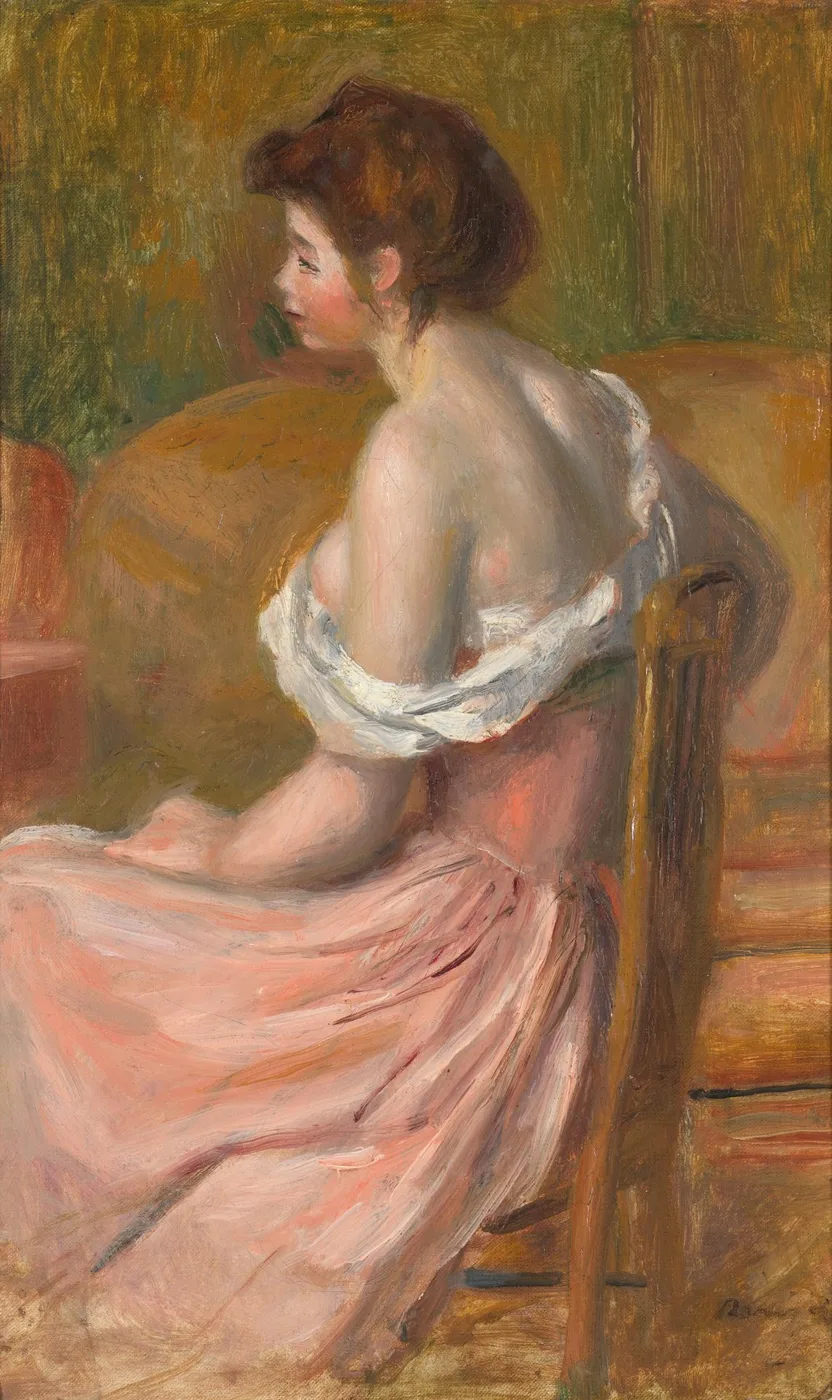 Seen from behind, a woman sits on a chair with her chemise slipped off her shoulders, a pink skirt pooling around her